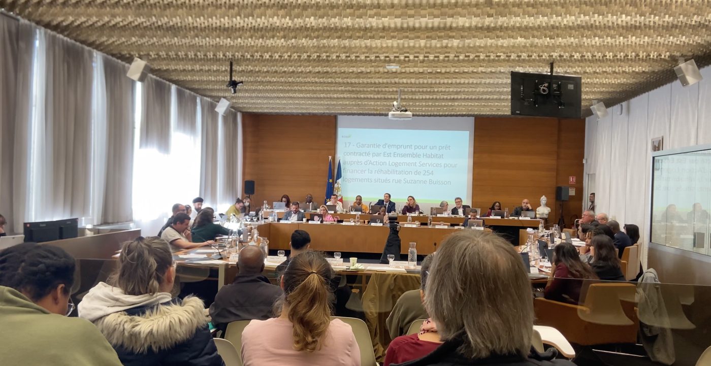 Séance du conseil municipal : élus autour de la table, public au premier plan, et un écran affichant le point 17 de l'ordre du jour